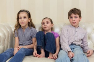 Three children sitting on a sofa and watching TV