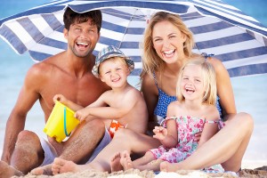 Family Sheltering From Sun Under Beach Umbrella