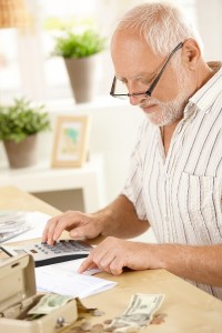 Older man concentrating on financial job, using calculator at ho